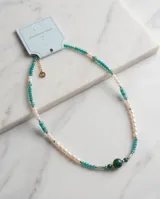 Collar de acero con baño de oro, compuesto por una combinación de perlas naturales blancas, piedras semipreciosas en tonos verdes y turquesas, y pequeñas cuentas doradas. Presenta un dije central de piedra verde oscura y un cierre con cadena de alargue que incluye una medalla grabada con las iniciales MA.