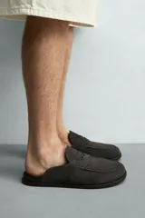 Zueco de hombre fabricado en piel con acabado serraje en color marrón claro. Presenta un diseño destalonado con detalle de antifaz en el empeine, horma redonda y suela plana a contraste.