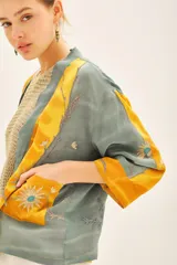 Kimono corto de viscosa con diseño estampado en tonos amarillo y gris, decorado con bordados en hilo de lurex. Presenta un corte holgado con mangas tres cuartos y un cinturón integrado de la misma tela.