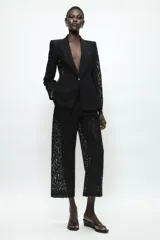 Pantalón de tiro alto confeccionado en encaje negro con diseño floral, de corte recto y largo cropped. Cuenta con forro interior a tono y cierre frontal con cremallera y ganchos metálicos.