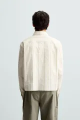 Camisa relaxed fit de manga larga con cuello solapa, confeccionada en tejido con mezcla de algodón. Presenta un estampado de rayas verticales en tonos beige, blanco y marrón. Incluye un bolsillo plastrón en el pecho, puños con botón y aberturas laterales en el bajo. Cierre frontal de botonadura.