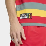 Remera Adidas Originals de corte ajustado con diseño de rayas horizontales en colores rojo, amarillo y verde. Presenta mangas cortas negras con las icónicas tres tiras blancas en los hombros, cuello redondo negro, logo del trébol bordado en el pecho y la inscripción 'Bob' en tipografía cursiva.