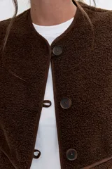 Chaleco de textura tipo corderito en color marrón chocolate, con cuello redondo, cierre frontal con botones y bolsillos laterales.
