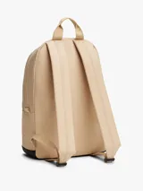 Mochila Tommy Jeans de diseño redondeado en color beige con base negra. Cuenta con compartimento principal con cierre de cremallera, bolsillo frontal con cierre, correas ajustables acolchadas y asa superior. Incluye parche distintivo de la marca en la parte frontal.
