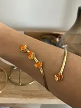 Brazalete abierto de metal dorado con acabado martillado, decorado con cuatro piedras de color naranja en bruto.