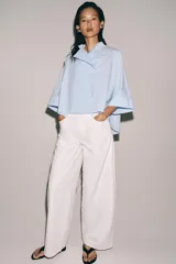 Camisa Zara Woman Collection de algodón con estampado de rayas verticales blancas y celestes. Presenta cuello perkins, mangas tres cuartos y un diseño asimétrico con cierre frontal cruzado mediante botones.