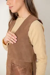 Chaleco de cuero marrón con diseño sin mangas, corte recto y bolsillos frontales con detalle metalizado en tono cobre. Presenta costuras decorativas en los bordes y en los bolsillos.