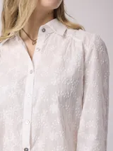 Camisa blanca de algodón con bordado floral, corte clásico, cuello camisero y mangas largas con puños abotonados.