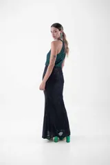 Vestido largo de fiesta con lentejuelas, compuesto por un top verde esmeralda con cuello halter y una falda negra ajustada con abertura lateral.