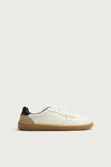Zapatillas deportivas barefoot de hombre elaboradas en piel. Diseño en color blanco con detalles en negro y beige en el talón, y suela plana de goma marrón.