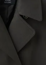Chaqueta estilo gabardina larga en color gris oscuro, con doble botonadura frontal, solapas clásicas, bolsillos y trabillas ajustables en los puños.