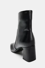 Botín de cuero sintético color negro, con diseño de punta cuadrada, cierre lateral mediante cremallera y tacón alto en bloque.