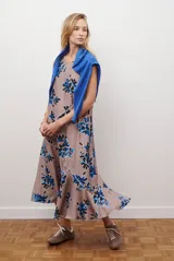 Vestido midi color beige con estampado de hojas en tonos azules y negros. Diseño sin mangas, cuello redondo y corte acampanado.