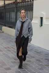 Chaqueta de punto con capucha, manga larga y cierre frontal con cremallera. Presenta un diseño en color beige con un lazo decorativo a contraste en color marrón oscuro en la zona del cuello.
