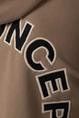 Buzo canguro oversize de frisa de algodón premium en color azul grisáceo. Presenta un diseño con recortes frontales, bolsillo tipo canguro y un pequeño logo circular estampado en el pecho. Cuenta con puños y ruedo acanalados.
