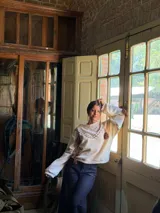 Buzo de punto color crema con diseño oversize, cuello redondo y mangas largas abullonadas. Presenta detalles de costuras decorativas en contraste y apliques de flecos colgantes en la parte frontal y mangas.