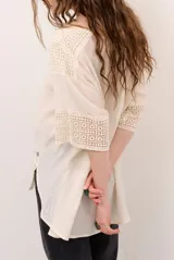 Blusa color blanco, de corte holgado y mangas tres cuartos, con detalles de encaje y bordados en las mangas y en el ruedo.