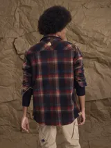 Sobrecamisa de tejido polar con estampado abstracto en tonos rojizos y azul marino. Presenta cuello clásico, cierre frontal con botones a presión, dos bolsillos frontales con solapa en el pecho y un parche decorativo.