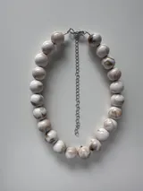 Collar corto compuesto por cuentas esféricas grandes con efecto marmolado en tonos marrones y dorados, con cadena de extensión plateada y cierre de mosquetón.