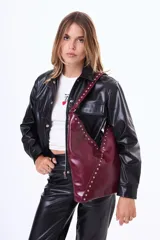 Bolso tipo hobo de cuero sintético negro con acabado brillante, decorado con tachuelas plateadas a lo largo de la correa y en el borde frontal. Presenta un diseño asimétrico en la parte superior.