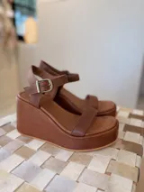 Sandalias de plataforma corrida color marrón con tira delantera simple, tira en el empeine y tira al tobillo con hebilla metálica.