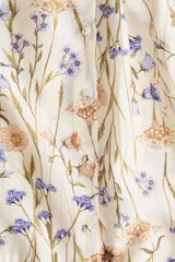 Vestido túnica evasé corto de color beige con estampado floreado en tonos azules y rosados. Cuenta con escote redondo amplio, botones forrados al frente y mangas raglán globo largas con puños elásticos. Presenta un diseño holgado con fruncido escalonado bajo la cadera.