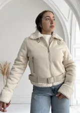 Chaqueta color crema con cuello y puños de piel sintética, cierre frontal con cremallera y cinturón ajustable en la cintura.
