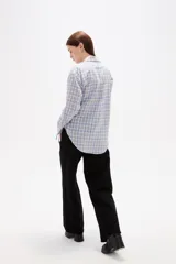 Camisa de poliéster con estampado a cuadros, cuello camisero, cierre frontal con botones y detalle de lazo ajustable en la cintura.