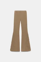 Pantalón de corte flare confeccionado en mezcla de algodón con efecto lavado. Presenta tiro medio, cintura elástica y detalles de tachas y aplicaciones bordadas en el bajo de las piernas.