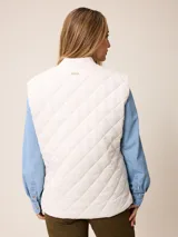 Chaleco acolchado de diseño matelassé con cierre frontal completo, cuello tipo bomber y bolsillos laterales. Presenta un pequeño bordado decorativo en la parte inferior.