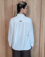 Camisa blanca de algodón con cuello alto tipo mao y volados sutiles a lo largo de la botonadura frontal. Presenta mangas largas con frunces en los hombros y botones frontales.