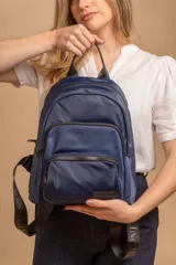 Mochila urbana de diseño funcional en color beige, confeccionada en tela impermeable. Cuenta con un compartimento principal amplio, un bolsillo secundario y un bolsillo frontal, todos con cierre. Incluye asa superior y correas ajustables para los hombros, con detalle de etiqueta de marca en el frente.