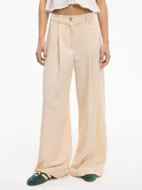 Pantalón de tiro alto y pierna ancha color beige con lunares pequeños. Tiene textura brillosa, bolsillos laterales, pretina con botón y pasacinto.