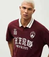 Remera de corte boxy confeccionada en piqué de algodón color bordó. Presenta cuello polo en color blanco con detalles en contraste, mangas cortas y estampa frontal con diseño gráfico y lettering en color blanco.