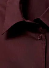 Camisa oversize de popelín de algodón en color bordó, con cuello camisero, manga larga con puños abotonados y cierre frontal de botones.