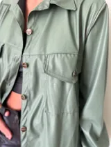 Camisa verde de cuero sintético con cuello clásico, cierre frontal con botones metálicos y dos bolsillos con solapa en el pecho.