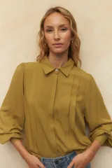 Camisa blanca de mangas abullonadas con sutiles plisados frontales, cuello clásico y corte relajado.