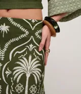 Pollera larga (midi/maxi) de tejido piqué, color verde oscuro con estampado en blanco/beige de motivos tropicales y palmeras. Presenta un diseño con fruncido en la parte inferior.