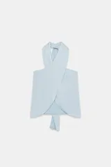 Top de cuello halter con diseño cruzado en el frente, confeccionado en tejido satinado. Presenta bajo asimétrico con detalle de lazada y cierre posterior con botones.