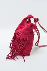 Cartera tipo bandolera color rojo oscuro, con flecos en la parte inferior y cierre de cremallera. Tiene una correa fina con un nudo decorativo.