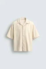 Camisa de corte relajado confeccionada en tejido de algodón, con cuello bowling y manga corta. Presenta un diseño con bordados geométricos a tono y cierre frontal de botones.