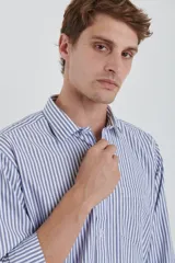 Camisa celeste y blanca a rayas verticales, de manga larga con puños abotonados y cuello clásico.