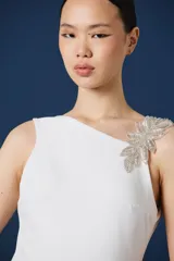 Vestido largo negro de corte sirena y silueta ajustada, con detalle de aplique floral brillante en el hombro izquierdo.