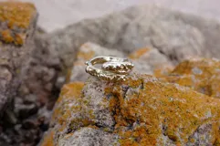 Anillo abierto de diseño orgánico con textura irregular y acabado brillante, realizado artesanalmente en metal.