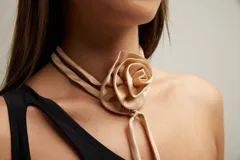 Gargantilla tipo choker de satén color beige con diseño de flor en el centro y tiras largas colgantes.