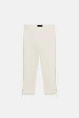 Pantalón capri de tiro alto en color crudo, con detalle de lazos ajustables en los bajos y cierre lateral con cremallera oculta.