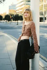 Cropped top de manga larga color marrón en punto estilo crochet con diseño en hilo de chenilla y ribetes festoneados. Cuenta con escote en U y botones forrados al frente, con forro de punto.