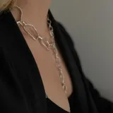 Collar de cadena con eslabones irregulares de diseño artesanal, con cierre frontal tipo barra y aro. La pieza permite diversas formas de uso, incluyendo como collar, pulsera o accesorio de espalda.
