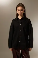 Sobrecamisa de jean color negro, con cierre frontal de botones metálicos, mangas largas y detalle de pequeñas tachas decorativas en la parte superior delantera.