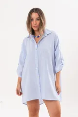 Vestido camisero de lino color celeste, con escote en V, cuello clásico, cierre frontal de botones y mangas tres cuartos regulables. Diseño holgado con corte asimétrico.